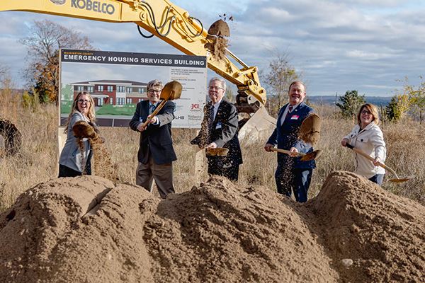 Board of Commissioners standing behind a mound of dirt with shovels at the EHSB groundbreaking